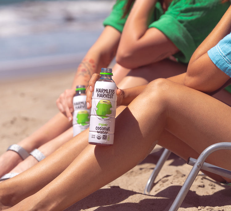 Two people enjoying Harmless Harvest Organic Coconut Water on beach