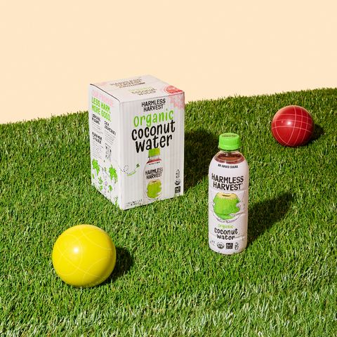 harmless harvest 4-pack of organic coconut water box next to a bottle of harmless harvest organic coconut water on grass in front of yellow background